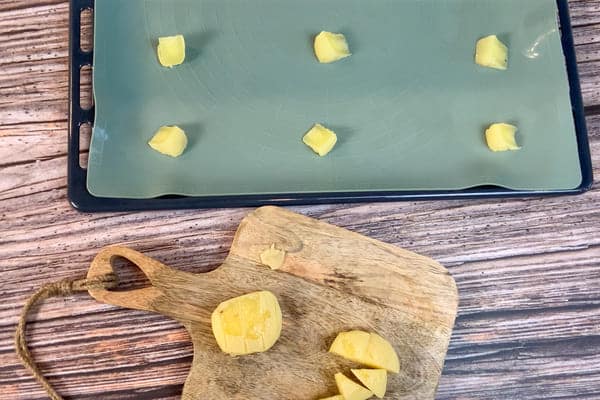 Harzer Käse Stücke mit viel Abstand auf einem Backblech und Harzer Käse auf einem Holzbrett