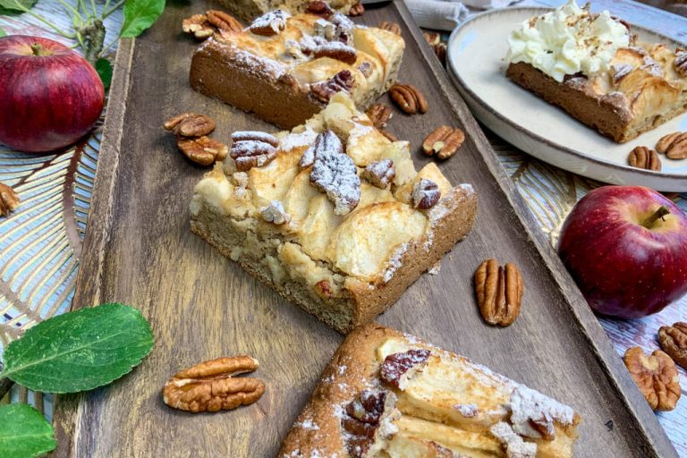 Low carb Apfelkuchen vom Blech in Stücken auf einem Holztablett mit Pekannüssen und frischen Äpfeln