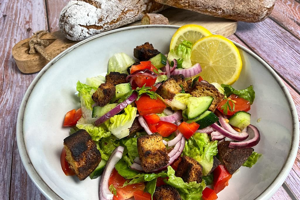 Low carb Brotsalat mit Croutons aus altem Eiweißbrot, Tomaten, roten Zwiebeln, Paprika und Gurken auf einem Teller